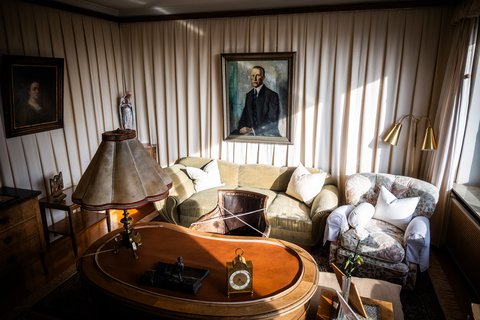 Gemütliches Wohnzimmer mit einem ovalen Holztisch, Sofas, einem gemalten Porträt an der Wand und weichen Tageslichtstrahlen.