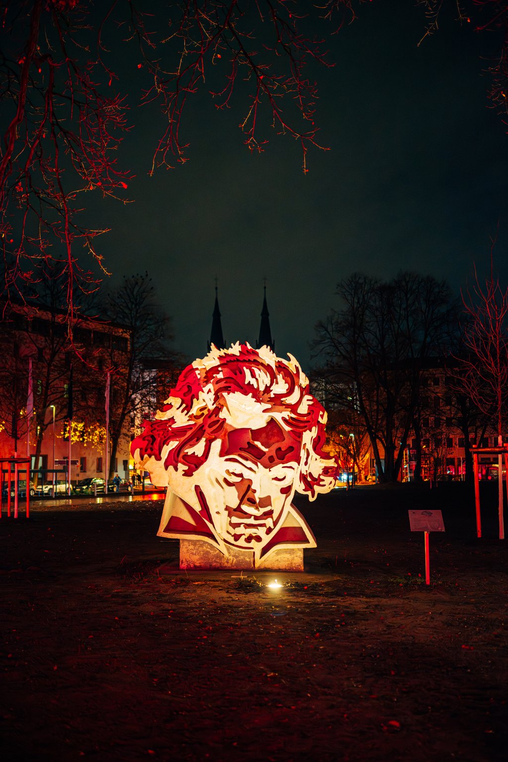 Eine leuchtende übergroße Skulptur von Beethovens Kopf bei Nacht, beleuchtet von roten Lichtern, vor einem dunklen, winterlichen Hintergrund.