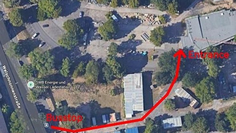 Luftbild einer Straße mit roter Linie, die die Route von einem Parkplatz zu einem Gebäudeeingang markiert.