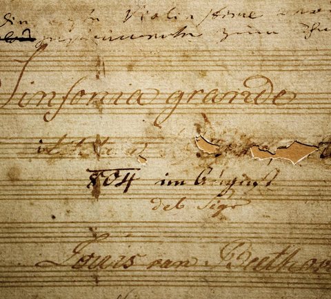 Nahaufnahme einer alten Partitur mit der Aufschrift "Sinfonia grande". Zart geschriebene Notizen und verblasste Linien sind sichtbar.