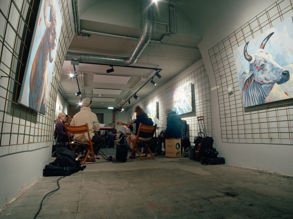 Eine Gruppe von Menschen sitzt in einer Galerie, umgeben von moderner Kunst. An den Wänden hängen große Gemälde.