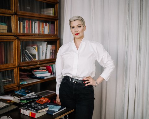 Eine Frau steht vor einem Bücherregal. Sie blickt in die Kamera. Ihre Haare sind kurz und sie trägt eine helle Bluse. Sie stützt den Arm in die Hüfte.  © Pasha Kritchko