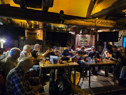 Eine Gruppe von Musikern spielt traditionelle Musik in einem gemütlichen Pub, umgeben von Holzmöbeln und sanfter Beleuchtung.