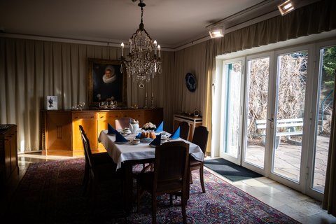 Ein elegantes Esszimmer mit einem Esstisch, gedeckt mit blauen Servietten. Ein Kronleuchter hängt von der Decke.