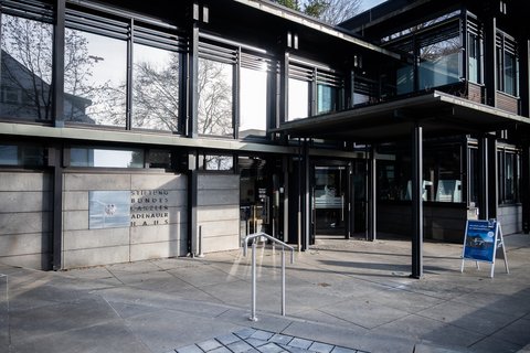 Moderner Museums- oder Galerieeingang mit Glasscheiben und Metallrahmen. Ein Freistehendes Schild steht vor dem Gebäude.