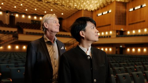Zwei Männer stehen in der leeren Beethovenhalle, blicken auf die Bühne. Die warme Beleuchtung schafft eine intime Atmosphäre.  © Nekame Klasohm
