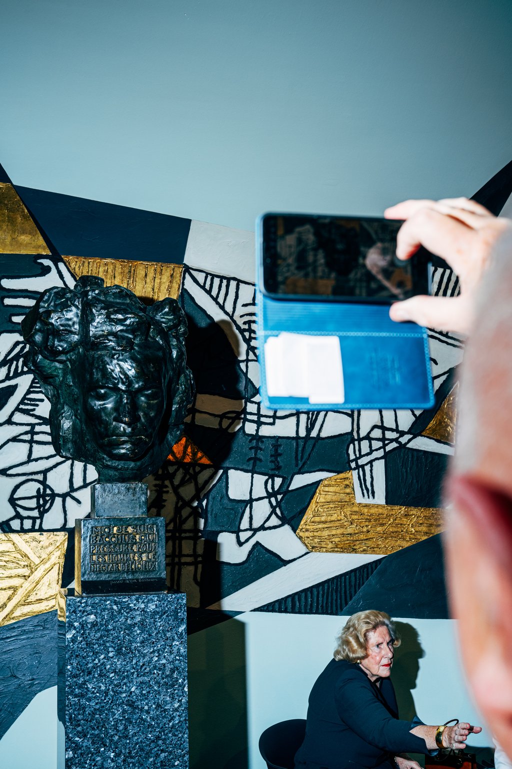 Ein Mensch hält ein Handy, um eine Skulptur in einem modernen Raum mit abstrakter Kunst an der Wand zu fotografieren.