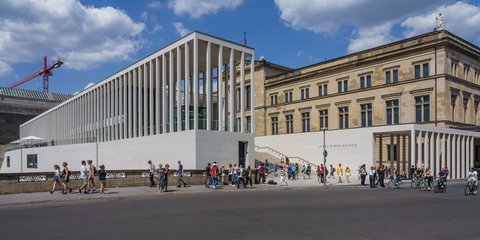 Das Foto zeigt ein modernes Gebäude mit Säulen und ein klassisches Gebäude. Menschen stehen davor unter einem blauen Himmel. ©A. Savin, wikimedia commons