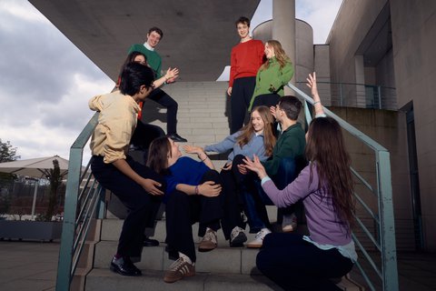 Eine Gruppe von Menschen in bunter Kleidung posiert kreativ auf einer Treppe, alle in lebhafter Haltung und miteinander interagierend.