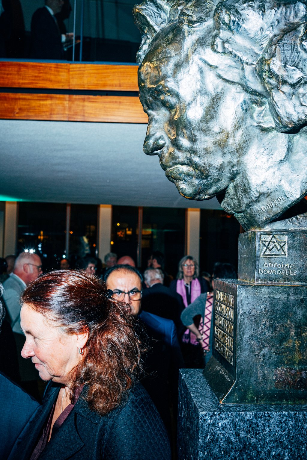 Personen stehen neben einer großen Büste von Beethoven mit energischem Gesichtsausdruck. Innenraum, Abendveranstaltung.