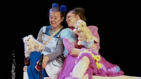 Zwei Schauspieler verkleidet in bunten Kostümen, einer in Blau, der andere in Rosa, halten Kuscheltiere und sitzen auf einer Bühne.  © Claus Overkamp