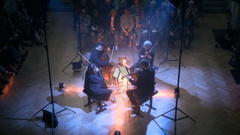 Ein Streichquartett spielt in einem dunklen Raum, umgeben von sitzendem Publikum. Stimmungsvolle Lichter beleuchten die Musiker von oben.  © Diana Lim