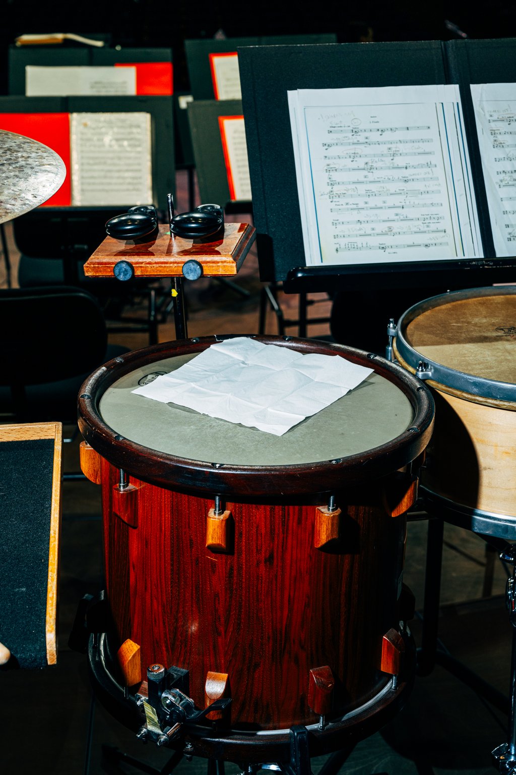 Orchesterbühne mit verschiedenen Notenständern und Trommeln. Ein Notenblatt liegt auf einer großen Trommel bereit.